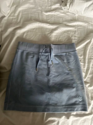 Ljusblå kortkjol med snörning - Säljer en ljusblå kortkjol med snörning i midjan och broderad logga nertill. Kjolen har en sportig känsla och är perfekt för dig som gillar en avslappnad men ändå snygg stil.