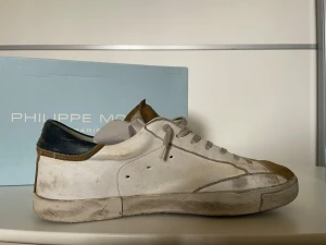 Philippe Model vita sneakers - Snygga vita sneakers från Philippe Model med beige mockadetaljer på tå och plös samt mörkblå häl. Klassisk låg modell med vita skosnören och diskret logga på sidan. Skorna har använts en del, och är slitna på några få ställen. Dock bör detta gå att fixas! Box medföljer, nypris ~ 3700 kr. Kom gärna med prisförslag!