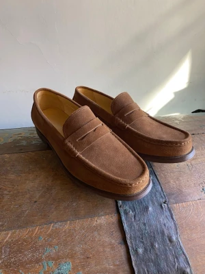 Bruna mockaloafers med klassisk design - Snygga loafers i brun mocka med klassisk pennyloafers-design. Skorna har rundad tå, låg klack och diskret söm längs ovandelen. Perfekta för dig som gillar stilrena och tidlösa skor.
