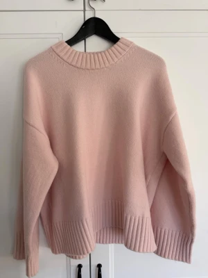 Ljusrosa oversized stickad tröja - Mysig ljusrosa stickad tröja med oversized passform och breda ribbade muddar vid ärmslut, nederkant och halsringning. Perfekt för lager på lager och en avslappnad look. Tröjan har droppade axlar och är tillverkad i ett mjukt material. Använt 1 gång 