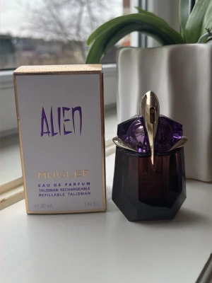 Alien Eau de Parfum från Mugler 30ml - Alien Eau de Parfum från Mugler i en unik, mörklila och guldfärgad flaska med futuristisk design. Flaskan rymmer 30 ml och är påfyllningsbar. Doften är ikonisk och mystisk, perfekt för dig som gillar att sticka ut.