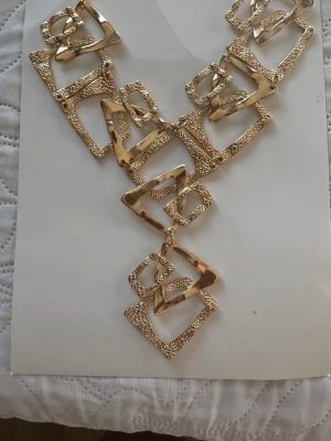 Ny. Guldigt statementhalsband med fyrkanter - Unikt halsband i guldton med stora, sammankopplade fyrkantiga länkar i olika storlekar. Halsbandet har både släta och strukturerade ytor som ger en cool och modern look. Perfekt för dig som vill sticka ut och addera lite edge till din outfit.