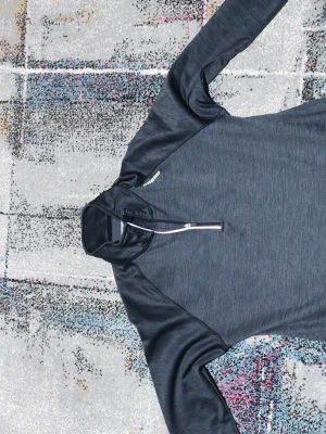 Mörkgrå träningströja från Karhu - Snygg mörkgrå långärmad träningströja från Karhu med halv dragkedja framtill. Tillverkad i mjukt och stretchigt funktionsmaterial med borstad fleece på insidan för extra komfort. Perfekt för löpning eller gymmet under kyligare dagar.