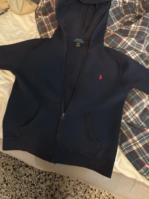 Marinblå tröja från Polo Ralph Lauren - Klassisk marinblå tröja från Polo Ralph Lauren med den ikoniska röda polospelaren broderad på bröstet. Tröjan har enkel design och är tillverkad i mjukt material som passar perfekt till en avslappnad stil. Nypris: 1250kr. Köpt på NK barnavdelning. Passar till allt du kan tänka dig, även riktigt grish!