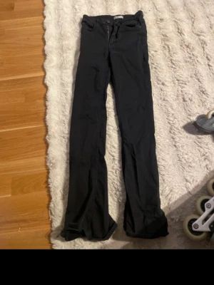Svarta bootcut jeans från Gina Tricot - Säljer ett par svarta bootcut jeans från Gina Tricot. Jeansen har klassisk femficksmodell, dragkedja och knapp framtill samt utsvängda ben. Materialet är mjukt och stretchigt för en bekväm passform. Perfekta till en trendig vardagslook. Ett hål de bild