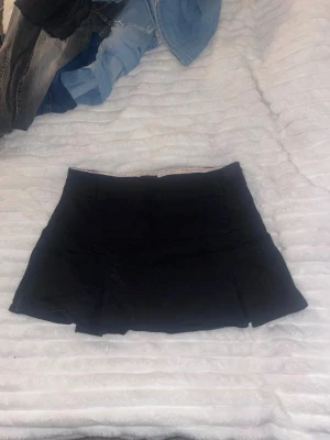 Svart kjol från att. i storlek 42 - Svart kjol från att. med klassisk rak passform och diskreta sömdetaljer. Insidan av linningen har ett gulligt blommigt mönster i rosa och grönt. Perfekt för dig som vill ha kjol-looken men med shortskomfort.