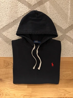 Svart Hoodie Från Polo Ralph Lauren - Hej! 👋 Säljer en riktigt snygg Polo Ralph Lauren hoodie i storlek L. 💎 Klassisk svart färg som passar till allt ✨ Väldigt fint skick i övrigt men har några små blekningar, främst på ena ärmen och vid huvan (se de sista bilderna för detaljer) 🎉 Grymt skön och sitter perfekt (Storlek L) 👕 Den klassiska röda broderade pony-loggan på bröstet 🐎 Alla tvättlappar sitter kvar för äkthetsverifiering ✅ Fraktar snabbt! 🚚📦 Hör av er vid frågor! 💬💯 