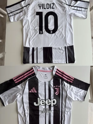 Juventus borta matchtröja Yildiz #10 - Juventus matchtröja från Adidas med Yildiz och nummer 10 på ryggen. Tröjan är vit med svarta ränder, rosa detaljer på axlarna och klubbmärke samt Jeep-logga på bröstet. Tillverkad i lätt och ventilerande material, perfekt för fotbollsträning eller match.