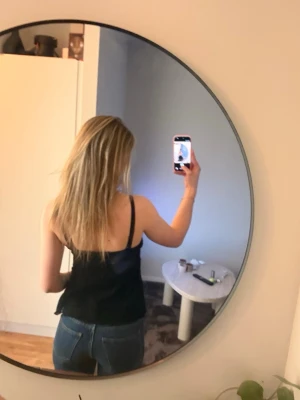 Svart spetslinnetopp med smala band - Säljer en svart linnetopp med smala axelband och v-ringning. Toppen har spetsdetaljer framtill och en lätt utsvängd passform som ger en avslappnad look. Perfekt att styla med jeans eller kjol