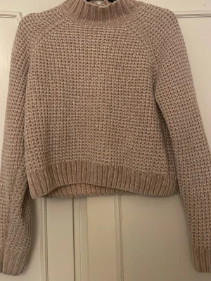 Beige stickad tröja med polokrage - Mysig beige stickad tröja med polokrage och grovstickad struktur. Tröjan har långa ärmar och ribbade muddar vid ärmslut och nederkant. Perfekt för kyliga dagar och enkel att matcha till olika outfits.