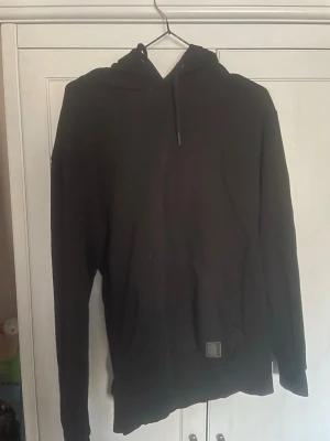 Svart hoodie från LCW CASUAL - En stilren svart hoodie från LCW CASUAL med klassisk huva och dragsko. Hoodien har lång ärm och är tillverkad i ett mjukt material som passar perfekt för en avslappnad look. Enkel design utan tryck eller mönster, vilket gör den lätt att matcha.