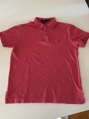 Rosa piké från Polo Ralph Lauren - Säljer en snygg rosa pikétröja från Polo Ralph Lauren i slim fit-modell. Klassisk krage, korta ärmar och knappar framtill. Ikoniska broderade loggan på bröstet. Perfekt till jeans eller shorts för en clean look. (STORLEK M I BARN SÅ EJ I VUXEN) Skriv om ni vill ha bild på hur den sitter.