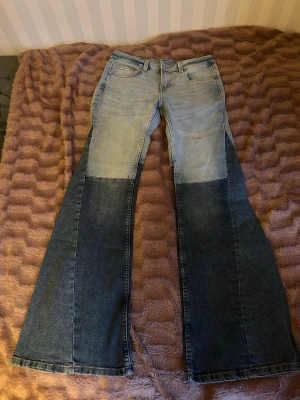 Tvåfärgade utsvängda jeans - Säljer ett par riktigt snygga tvåfärgade jeans med ljusblå överdel och mörkblå nederdel. Jeansen har utsvängda ben och klassisk femficksmodell. Perfekta för dig som vill sticka ut med en unik stil. Materialet är denim.