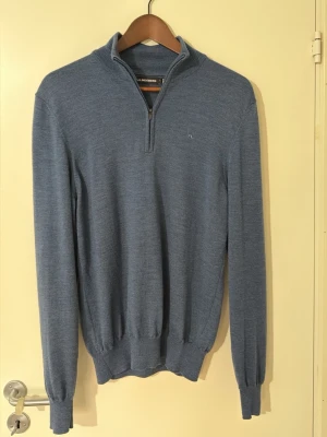 Blå halvzip-tröja från J.Lindeberg - Snygg blå stickad tröja från J.Lindeberg med halv dragkedja och liten broderad logga på bröstet. Stickad i 100% merino ull, använt fåtal gånger så den är i nyskick. Djur och rökfritt hem, nypris 1600