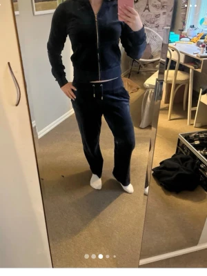 Juicy couture set - Mysigt loungewear-set i mörkblå velour med dragkedja framtill på tröjan och huva. Byxorna har resår i midjan och dragsko för skön passform. Perfekt för chill dagar hemma eller när du vill vara extra bekväm.