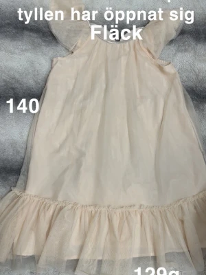 tyllklänning med volang - Söt aprikosfärgad klänning i tyll med volangkant nedtill och puffiga ärmar. Klänningen har en mjuk, luftig känsla och är perfekt för dig som gillar romantisk stil. Passar till sommarens alla tillfällen.🌸 Fläck samt att en bit på tyllens söm har gått upp. Storlek 140 