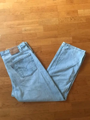 Ljusblå Levi's raka jeans - Säljer ett par klassiska ljusblå Levi's jeans i rak modell. Jeansen har fem fickor, bälteshällor och den ikoniska läderpatchen bak i midjan. Tillverkade i slitstark denim med vintage vibe och snygg tvätt. Perfekta för en avslappnad och trendig look.