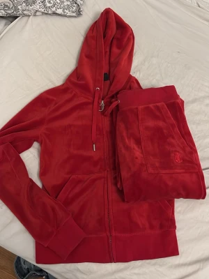 Rött velourset med hoodie och byxor - Mysigt loungewear-set i röd velour med matchande hoodie och byxor. Hoodien har dragkedja, fickor och justerbar huva med snören. Byxorna har resår i midjan och fickor. Perfekt för chill dagar hemma.