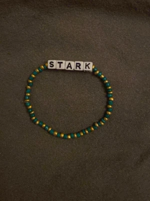 Pärlarmband med texten STARK - Fint handgjort armband med små gröna och gula pärlor samt vita bokstavspärlor som stavar STARK. Elastisk tråd gör det enkelt att ta på och av. Perfekt accessoar för dig som vill bära ett peppande budskap.