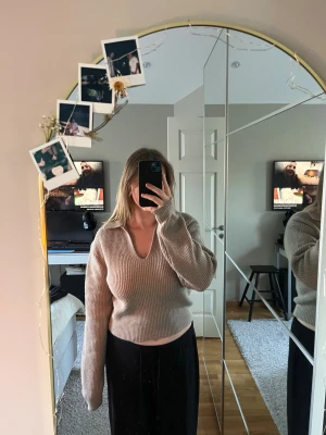 Beige stickad tröja med v-ringning - Säljer en beige stickad tröja med djup v-ringning och bred krage. Tröjan är ribbstickad och har långa ärmar med avslappnad passform. Perfekt för lager-på-lager och enkel att matcha med olika outfits.