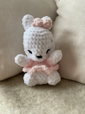 Liten virkad kanin - En liten handvirkad kanin, med klänning och rosett av mjukt chenillegarn. Mjukisdjuret är stoppad med polyesterfyllning och har säkerhetsögon av plast. Kaninen är ca 18 cm hög 🧶🐰 OBS! Pga plastögonen rekommenderas inte mjukisdjuret för barn under 3 år