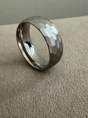 Titanium Ring 8mm – Borstad och hamrad yta - Titanium ring med -brushed/hamered finish - som ger en diskret men lyxig look. Passar för dig som gillar minimalistisk design med edge.    Material: Titanium (stämpel i ringen) Färg: Silver   Design: Handgjord, Borstad och hamrad yta, Bekväm passform, Unisex Bredd: 8 mm   Storlek: 19,8 mm i innerdiameter (US 10) Frakt: Alltid snabb leverans   💫 Finns även med 6mm bredd av samma modell. Se mina övriga annonser 💫