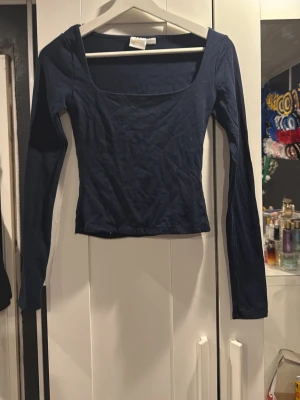 Mörkblå långärmad topp med fyrkantig ringning - Snygg mörkblå långärmad topp med fyrkantig ringning och tight passform. Perfekt att styla med jeans eller kjol för en trendig look. Gjord i mjukt bomullsmaterial som känns skönt mot huden.