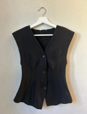 Svart kostymtopp - Säljer en jättefin svart kostymtopp från Zara i storlek S! Köpt på vinted för 255kr men har tyvärr bara kommit till användning en gång! Plagget har 3 svarta knappar framtill och är v- ringad med fina sömmar! Är väldigt snyggt att bli stylat med ett par jeans/kostymbyxor och smycken! Skriv gärna om du har några frågor pris kan diskuteras!