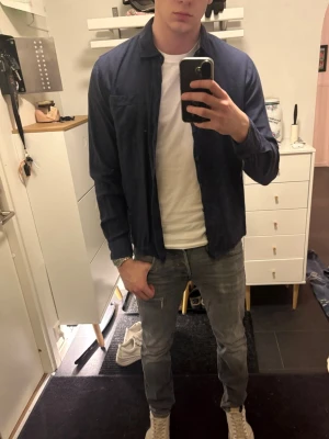 Mörkblå skjorta - Snygg mörkblå skjorta i. Klassisk krage, bröstficka och knäppning framtill. Skjortan har lång ärm och en avslappnad passform, perfekt att bära öppen över en t-shirt.