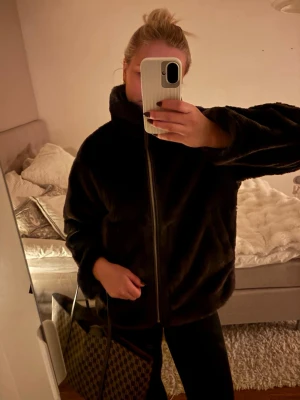 Svart teddyjacka med hög krage - Mysig svart teddyjacka med hög krage och dragkedja framtill. Jackan har en oversize passform och är gjord i mjukt, fluffigt material som ger en cool och avslappnad look. Perfekt för att hålla sig varm under kyliga dagar.