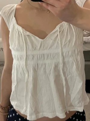 Vit linnetopp från 157 med knyt - Söt vit linnetopp från 157 med knytband vid halsringningen och lätt rynkad struktur. Toppen är ärmlös och har en luftig, avslappnad passform – perfekt nu till vår och sommar💕 