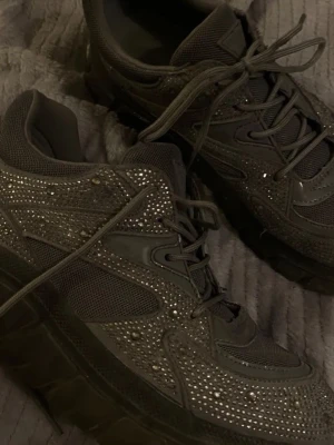 Grå glittriga sneakers från Guess - Snygga grå sneakers från Guess med massor av små glittrande stenar över hela skon. Köptes för 1599kr men säljer för billigare då jag vill bli av med de då jag använda ett fåtal gånger. ‼️‼️Kan gå ner i pris vid snabb affär. Kan hämtas upp k stockholm annars tillkommer frakt‼️‼️‼️