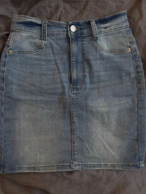 Blå jeanskjol - Snygg blå jeanskjol från Bubbleroom med klassisk femficksdesign, bälteshällor och knappstängning framtill. Kjolen är kort och har en rak passform, perfekt till vardagslooken. Tillverkad i bomull för en bekväm känsla.