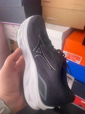 Svarta Mizuno sneakers med vit sula - Snygga svarta sneakers från Mizuno med vit, chunky sula och ventilerande mesh-ovandel. Skon har Mizuno-logga i silver på sidan och svarta skosnören. Perfekt för dig som gillar sportig och stilren look.
