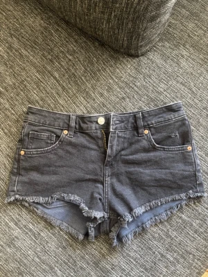 Grå jeansshorts med fransig kant - Snygga grå jeansshorts med fransig kant och klassisk femficksdesign. De har normal passform, bälteshällor och dragkedja framtill. Perfekta för varma dagar! Storlek 34💞