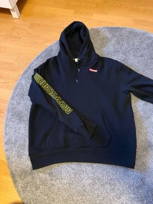 Levi's x Star Wars svart hoodie - Säljer en svart hoodie från Levi's i samarbete med Star Wars. På ärmarna står det 'GGWWWRGH!!!' i gult och på ryggen finns ett stort tryck av Chewbacca. Klassisk känguruficka och dragsko i huvan. Perfekt för dig som gillar coola prints och Star Wars.