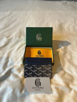 Mörkblå G korthållare - Snygg mörkblå korthållare med det klassiska mönstret i vitt och grått. Tillverkad i canvas och läder, perfekt för kort och ID. Kommer med originalask och certifikat. En stilren accessoar för dig som gillar exklusiva detaljer.