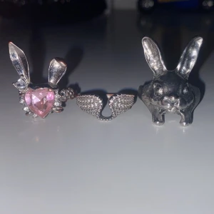 Set med tre silverfärgade ringar - Säljer ett set med tre unika ringar i silverfärg. En ring har kaninöron och rosa hjärtformad sten, en har små gnistrande vingar och den tredje har ett stort kaninhuvud med långa öron. Perfekta för dig som gillar statement-smycken och lekfull design.