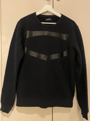 Svart sweatshirt från Crocker Stockholm - Svart sweatshirt från Crocker Stockholm med ett stilrent, blankt mönster framtill. Tröjan har rund halsringning, ribbade muddar vid ärmslut och nederkant samt en mjuk insida. Perfekt för en clean och avslappnad look. Regular fit