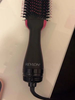 Revlon One-Step Volumiser hårfönborste - Revlon One-Step Volumiser är en svart och rosa elektrisk hårfönborste med rund form och borst i plast. Perfekt för att både torka och styla håret samtidigt. Ergonomiskt handtag och sladdanslutning för enkel användning. Endast testad 1 gång.