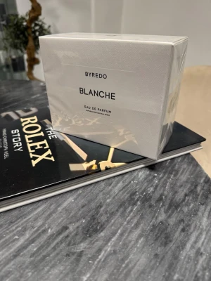 Byredo Blanche Eau de Parfum - Byredo Blanche Eau de Parfum i elegant vit kartong med subtilt mönster. Doften är känd för sin fräscha och rena karaktär, och flaskan levereras i originalförpackning. Perfekt för dig som gillar minimalistisk och stilren design.