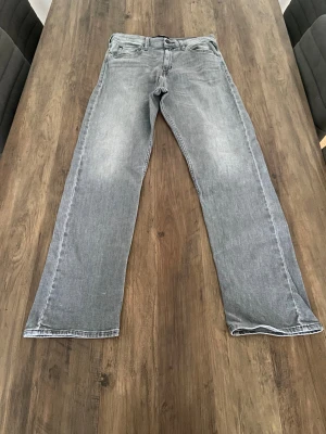Replay ljusgrå raka jeans - Snygga ljusgrå jeans från Replay med klassisk femficksdesign och raka ben. Jeansen har svarta broderade detaljer på bakfickorna och en tydlig Replay-logga på linningen. Tillverkade i mjukt bomullsmaterial för skön passform. Replay-Modellen är THAD
