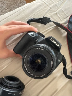 Canon EOS systemkamera med zoomobjektiv - Säljer en svart Canon EOS systemkamera med ett 18-55mm zoomobjektiv. Kameran har klassisk design med greppvänligt handtag och tydliga reglage. Objektivet är av plast och glas, perfekt för både foto och video. Rem och objektivlock medföljer.