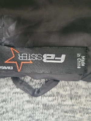 Mörkgrå dunväst med huva från EU SISTER - Snygg mörkgrå dunväst från EU SISTER med quiltad design och en mjuk, ljusgråmelerad huva. Västen har en modern passform och är perfekt för lager-på-lager-stil. Materialet är vadderat för extra värme och komfort.