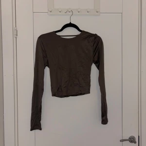 Brun croppad långärmad topp - Trendig brun croppad topp med långa ärmar och rund halsringning. Toppen har en öppen ryggdetalj som ger en snygg twist. Perfekt att styla med höga jeans eller kjol för en cool look.