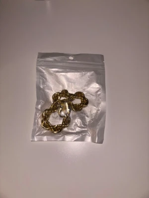 Cordell armband (Guld 10mm 20cm) - Säljer ett snyggt guldfärgat halsband med tvinnad kedja. Halsbandet har en robust karbinhake och känns riktigt trendigt. Perfekt accessoar för att lyfta din outfit med en touch av guld. Kommer i en praktisk plastpåse.