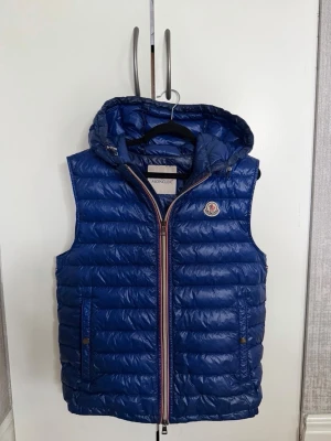 Moncler väst blå - Limited Edition. Moncler väst för herr i storlek M, moncler size 2. Passar även bra på S. Väst i blå färg. Modellen har luva, dragkedja framtill och sidofickor. Skriv för fler frågor, mvh.  Pris: 2599kr