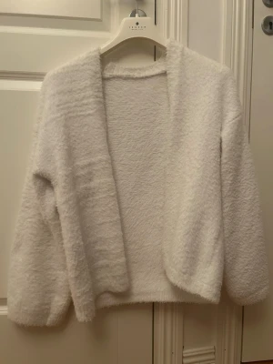 Vit fluffig kofta - Supersöt vit kofta i fluffigt material. Koftan har öppen front utan knappar, lång ärm och en avslappnad passform💓