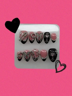 Rosa och svarta press-on naglar med dekorationer - Handgjorda lösnaglar i storlek S! Säljer ett set press-on naglar i rosa och svart med coola 3D-metalldekorationer som hjärtan, kedjor och bokstäver. Naglarna har en spetsig form och ger en edgy vibe. Perfekt för dig som vill sticka ut med din nagelstil!