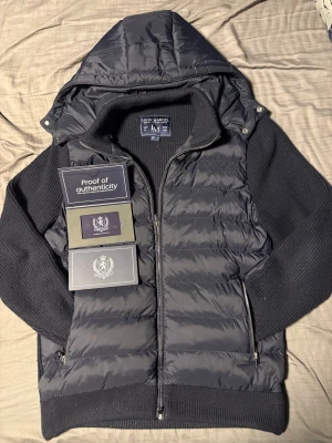 Mörkblå Cardigan från Leon Marcel - Mörkblå från Leon Marcel med stickade ärmar och huva. Framsidan är quiltad med dragkedja och sidofickor. Materialmix: nylon framtill, stickad bomull/ull/polyamid på ärmar och rygg, polyesterfyllning. Snygg, modern look med ribbade muddar och detaljer.